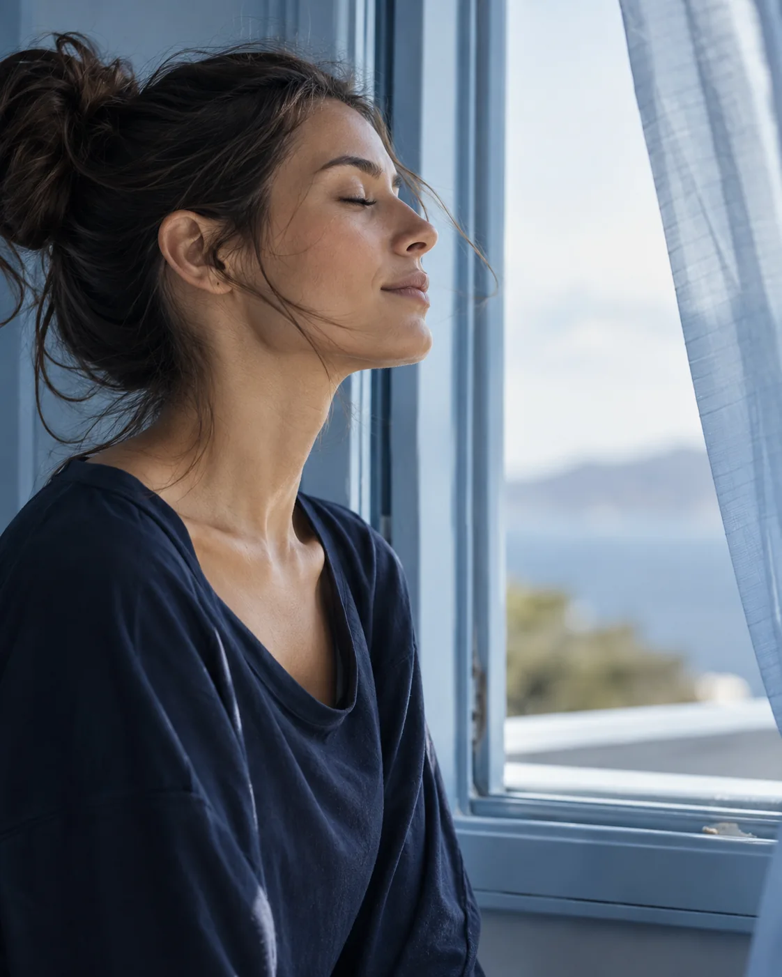 Woman pausing for an easy breath beside a light-filled window.