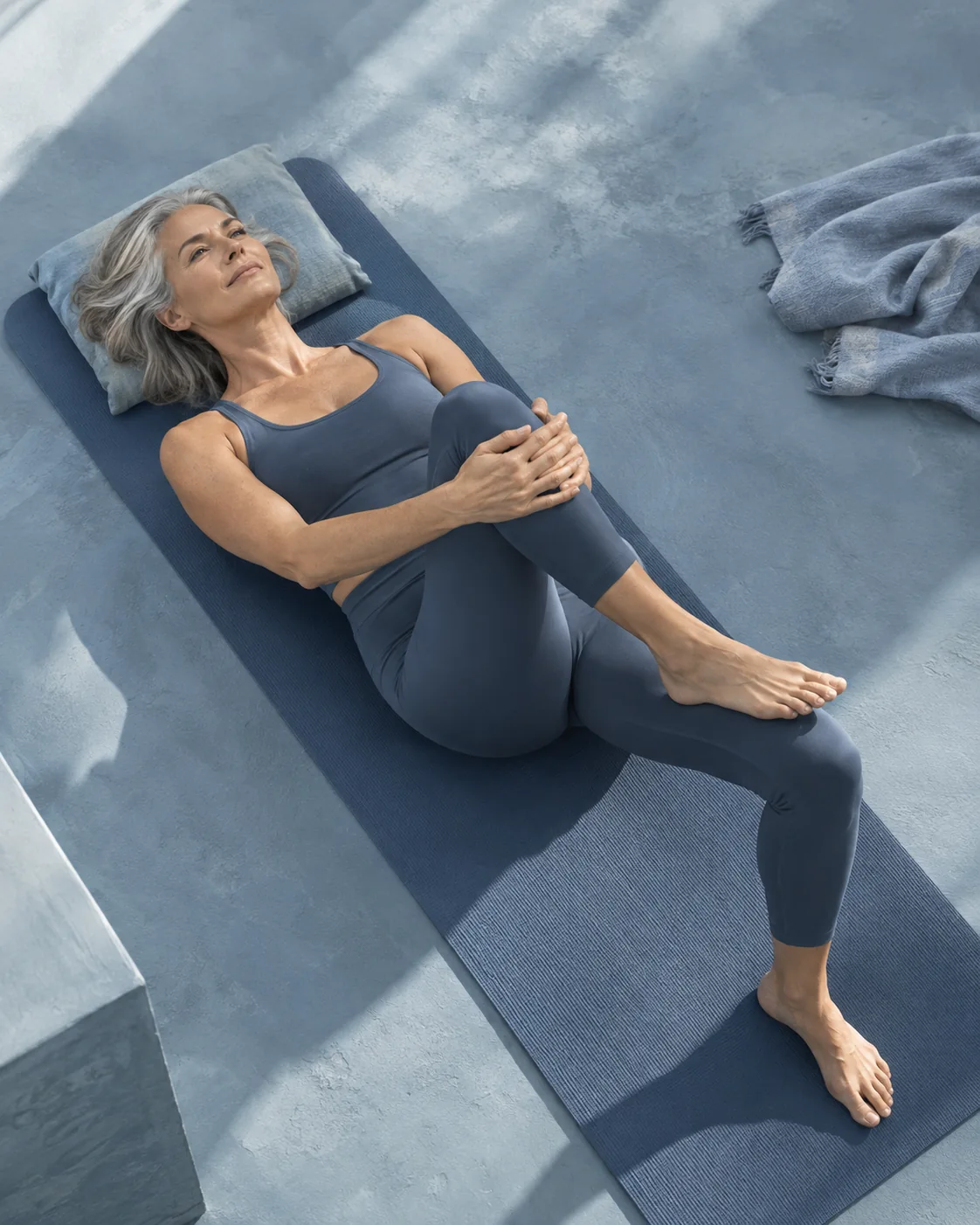 Woman gently drawing one knee toward her body while resting on a mat.